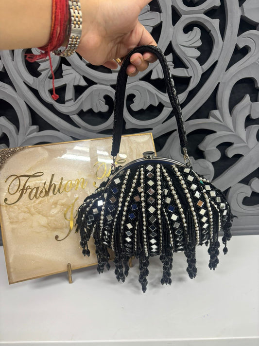 Black beaded handbag held by a hand with a decorative background