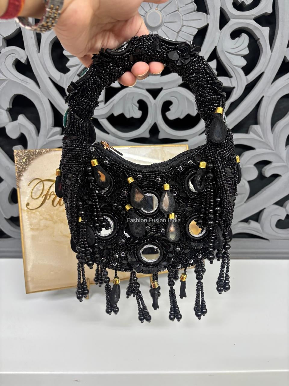 Black beaded handbag held by a hand with a decorative background