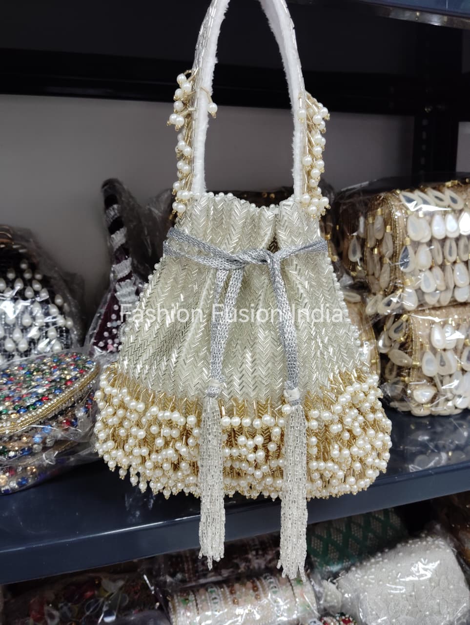 Pearl-handled handbag with decorative elements on a shelf with other bags.