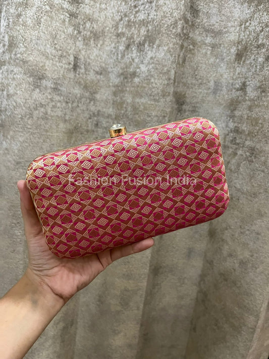 Hand holding a pink patterned clutch against a textured gray background