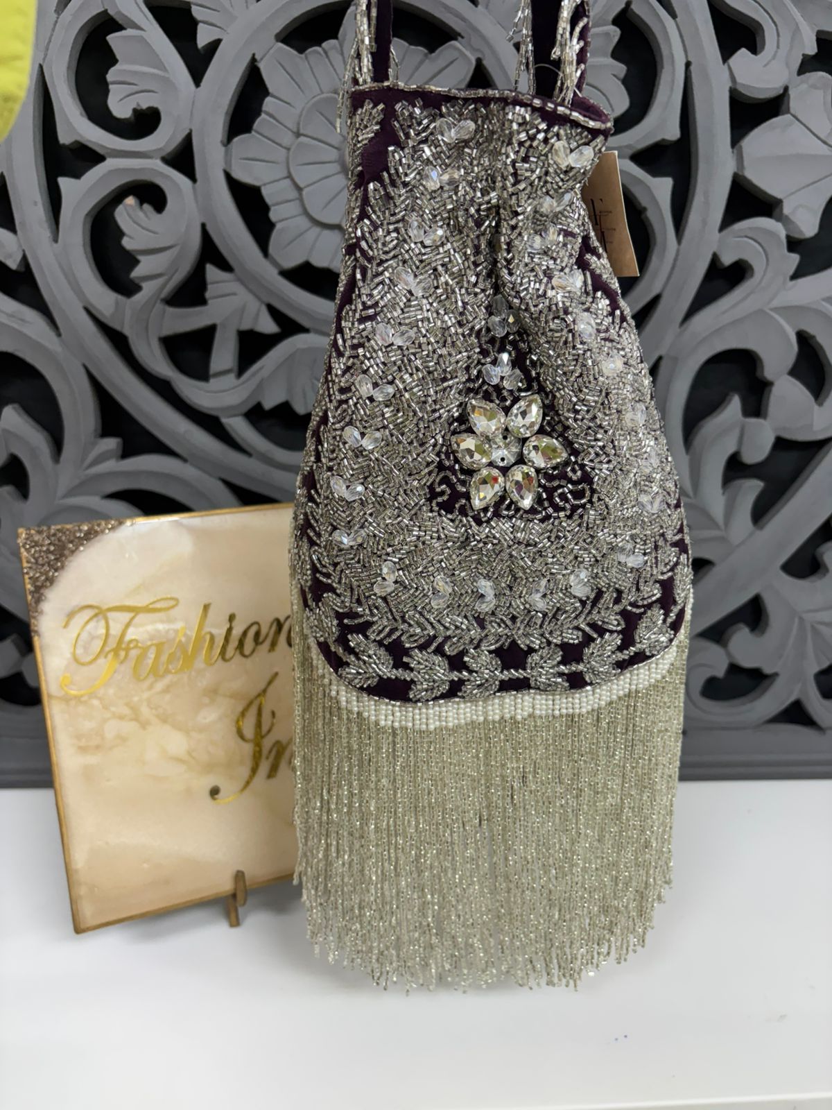 Decorative handbag with beaded details and tassels on a white surface with a decorative background.