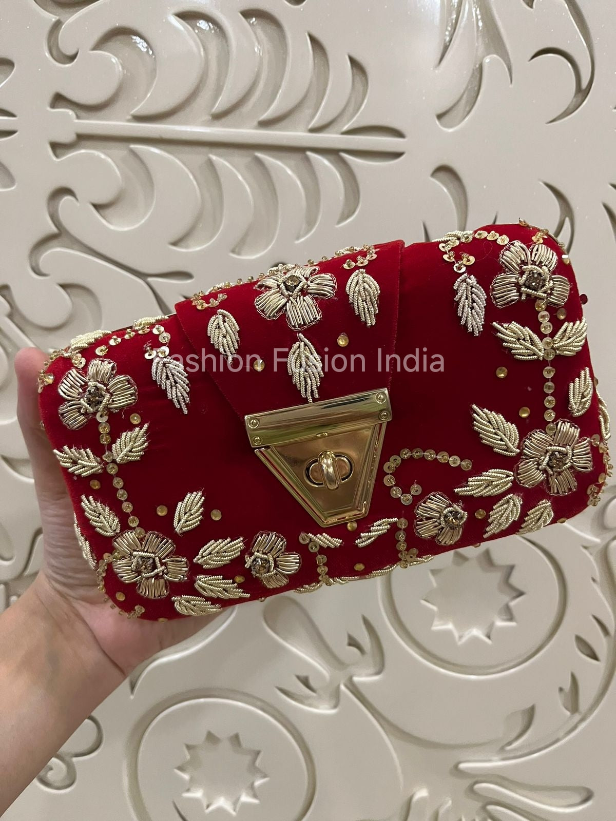 Red clutch bag with gold embroidery held against a decorative white background