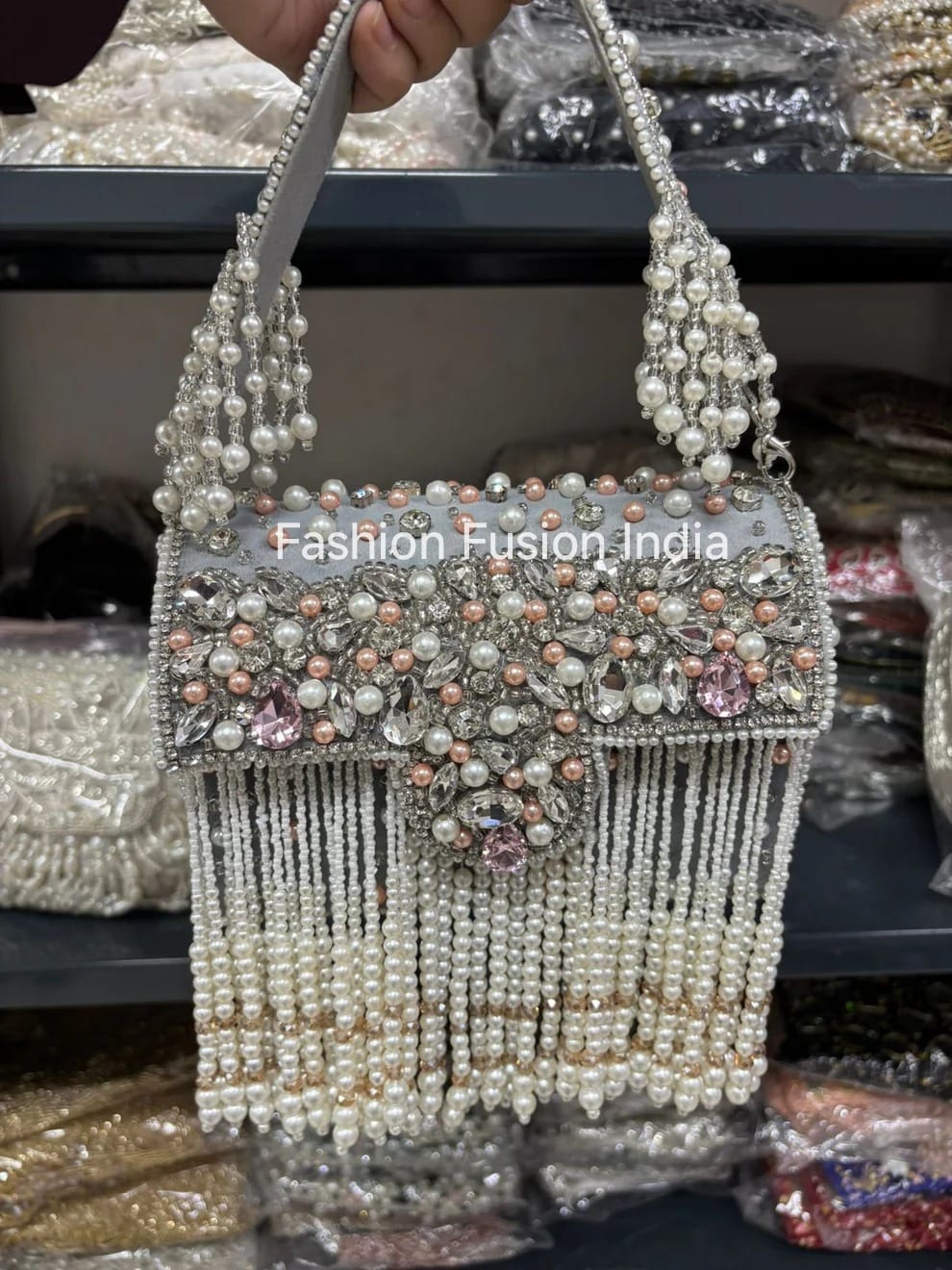Decorative handbag with beads and crystals held by a hand, with 'Fashion Fusion India' branding.