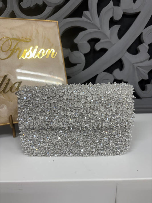 Silver clutch bag with rhinestone embellishments on a white surface with decorative background