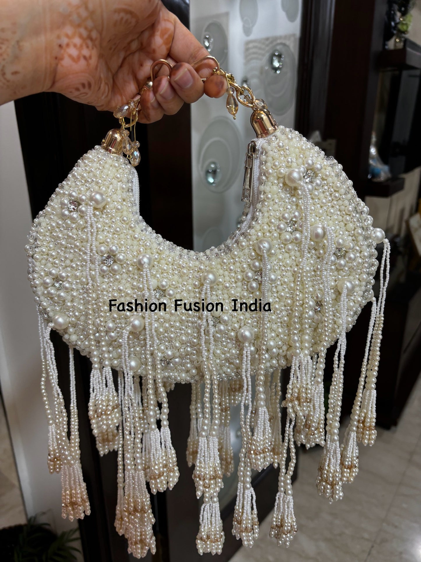 A white clutch bag with pearl embellishments and a textured surface, held up against a reflective background.