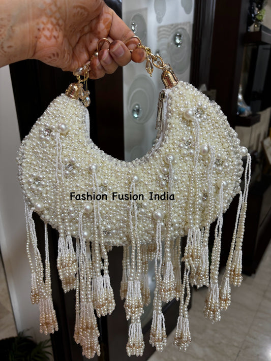 A white clutch bag with pearl embellishments and a textured surface, held up against a reflective background.